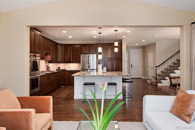 kitchen featuring a breakfast bar, light stone counters, decorative light fixtures, stainless steel appliances, and a kitchen island with sink