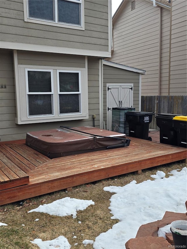 snow covered deck featuring a covered hot tub and fence