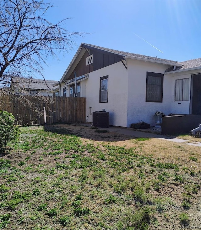 view of side of home with stucco siding, central AC, and fence