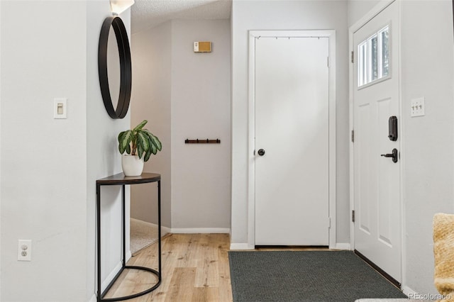 foyer with light wood-type flooring, baseboards, and a textured ceiling