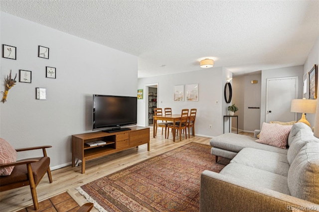 living room with baseboards, a textured ceiling, and light wood-style floors