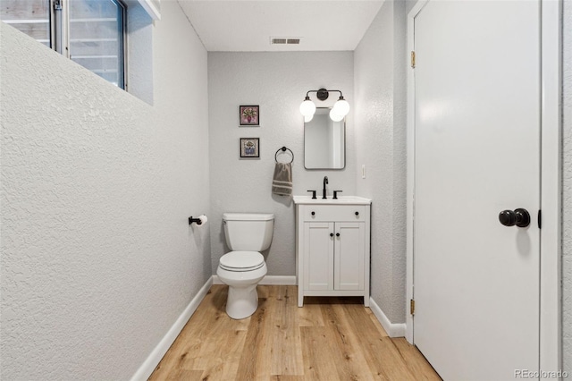 bathroom with vanity, wood finished floors, baseboards, toilet, and a textured wall