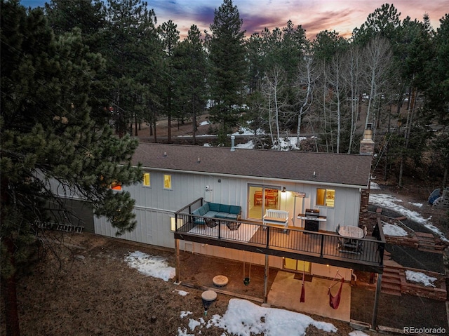 back of house at dusk featuring a deck, a chimney, and a shingled roof