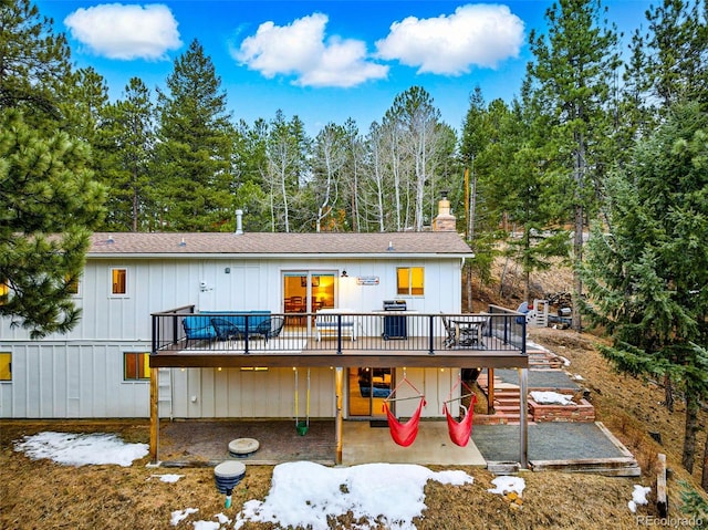 back of property featuring a shingled roof, a wooden deck, stairs, a chimney, and a patio area