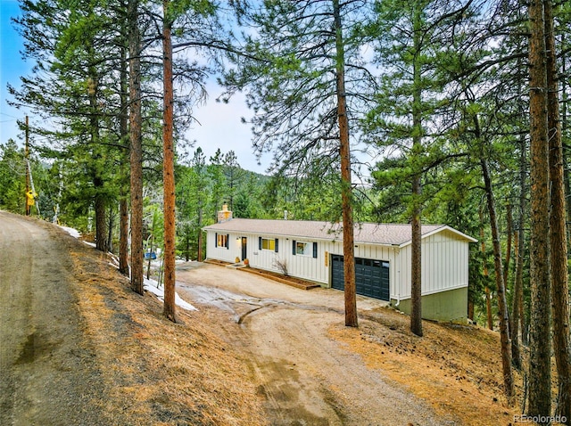 ranch-style house with a garage, board and batten siding, a chimney, and driveway