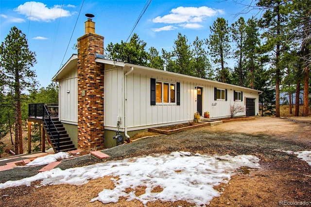 view of front of property featuring driveway, a chimney, stairs, a garage, and board and batten siding