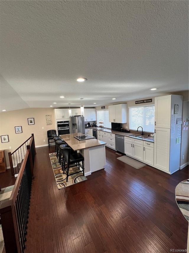 kitchen with appliances with stainless steel finishes, a center island, a kitchen bar, dark hardwood / wood-style floors, and white cabinets