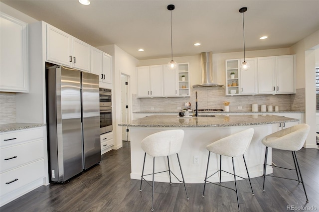 kitchen with appliances with stainless steel finishes, wall chimney exhaust hood, an island with sink, and white cabinets