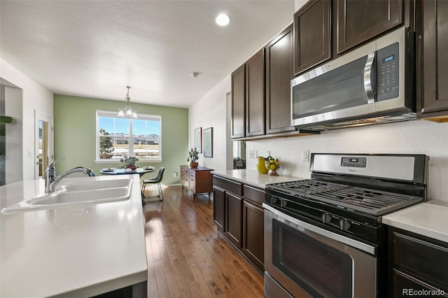 kitchen with sink, dark brown cabinets, hanging light fixtures, dark hardwood / wood-style floors, and stainless steel appliances