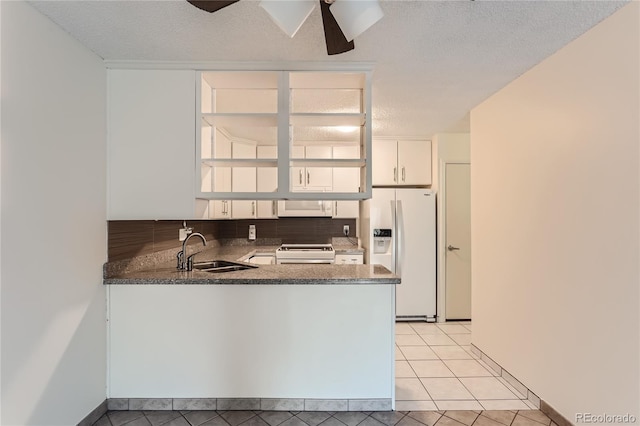 kitchen featuring stove, a textured ceiling, sink, white refrigerator with ice dispenser, and white cabinetry