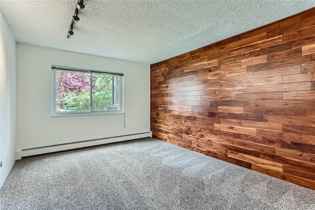 carpeted spare room with a textured ceiling, wooden walls, track lighting, and a baseboard heating unit