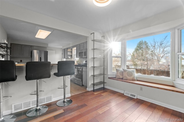 kitchen with hardwood / wood-style flooring, appliances with stainless steel finishes, a breakfast bar, and gray cabinetry