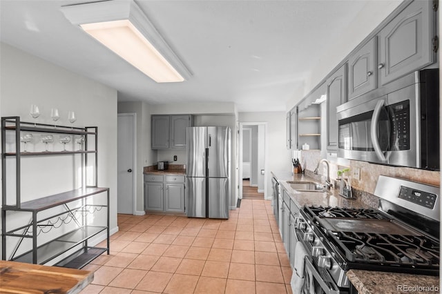 kitchen with gray cabinets, light tile patterned flooring, appliances with stainless steel finishes, sink, and light stone countertops