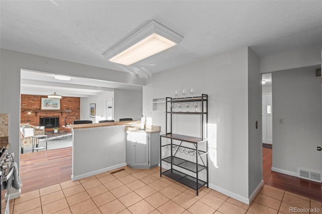 kitchen with light tile patterned floors, stainless steel stove, kitchen peninsula, and a brick fireplace