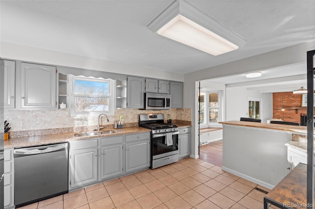 kitchen with tasteful backsplash, sink, gray cabinetry, light tile patterned floors, and stainless steel appliances