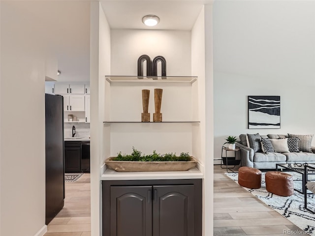 bar featuring light hardwood / wood-style flooring, sink, black appliances, and white cabinetry