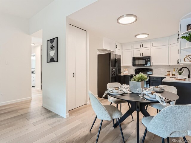 kitchen with light hardwood / wood-style flooring, white cabinets, black appliances, backsplash, and sink