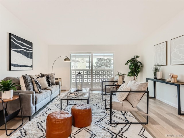 living room with vaulted ceiling, a baseboard heating unit, and light hardwood / wood-style flooring