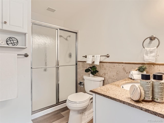 bathroom with toilet, a shower with door, tile walls, vanity, and hardwood / wood-style floors