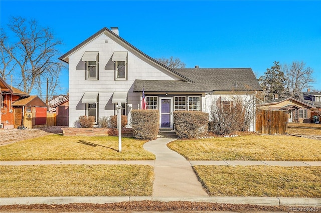 view of front of home featuring roof with shingles, a chimney, a front yard, and fence