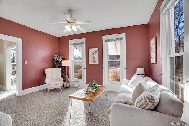 carpeted living area with ceiling fan and baseboards