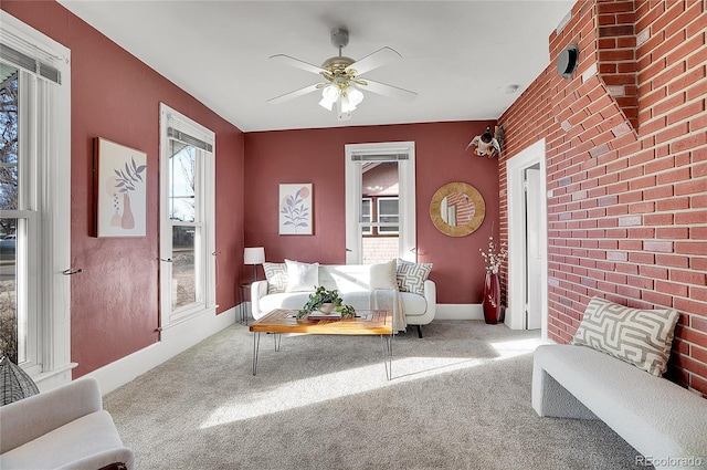 carpeted living area featuring brick wall, an accent wall, baseboards, and ceiling fan