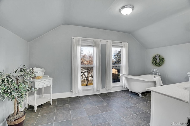 bathroom with a soaking tub, vaulted ceiling, vanity, tile patterned flooring, and baseboards