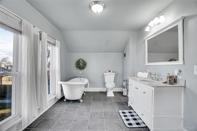 bathroom with lofted ceiling, vanity, baseboards, a freestanding bath, and tile patterned floors