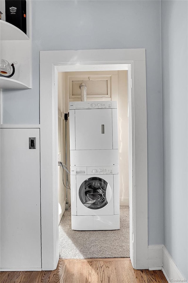 clothes washing area featuring light wood-type flooring, laundry area, and stacked washing maching and dryer