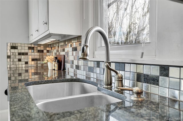 details featuring decorative backsplash, dark countertops, a sink, and white cabinets