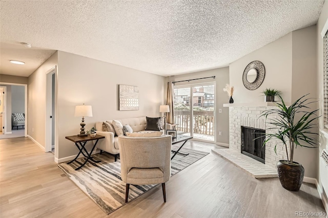 living area with light wood-style floors, a brick fireplace, a textured ceiling, and baseboards