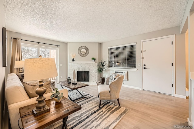 living room featuring light wood-style flooring, a fireplace, a textured ceiling, and a wall mounted air conditioner