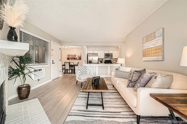 living room featuring an AC wall unit, baseboards, a textured ceiling, and light wood finished floors