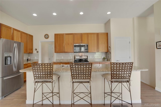 12348 W Gould Ave, Littleton, CO 80127 - kitchen featuring appliances with stainless steel finishes, backsplash, an island with sink, light stone counters, and a breakfast bar