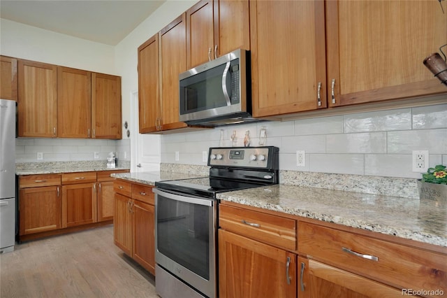 12348 W Gould Ave, Littleton, CO 80127 - kitchen with stainless steel appliances, backsplash, brown cabinetry, light wood-style floors, and light stone countertops