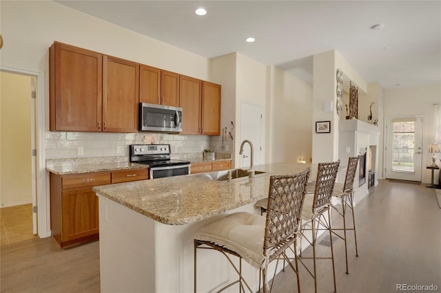 12348 W Gould Ave, Littleton, CO 80127 - kitchen with stainless steel appliances, a sink, tasteful backsplash, light wood finished floors, and light stone counters