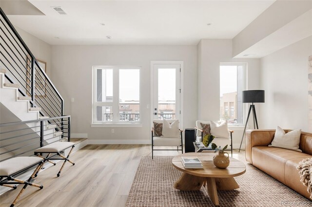 living area featuring light wood finished floors, plenty of natural light, stairs, and baseboards