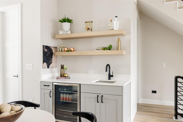 indoor wet bar featuring wine cooler, light wood-type flooring, and baseboards