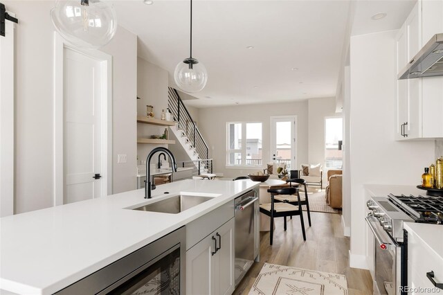 kitchen with a sink, stainless steel appliances, open floor plan, light countertops, and light wood finished floors