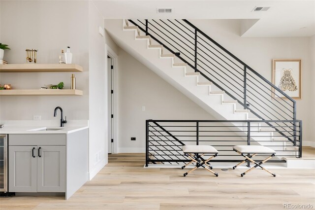 bar with light wood-style floors, a sink, beverage cooler, and baseboards