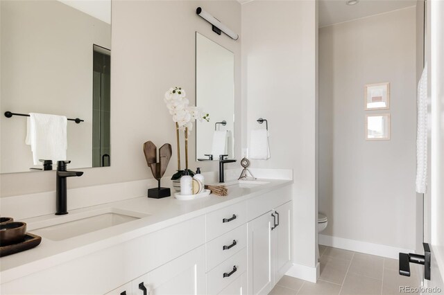 bathroom with toilet, double vanity, tile patterned flooring, and baseboards