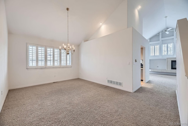 carpeted empty room featuring ceiling fan with notable chandelier, a fireplace, and high vaulted ceiling