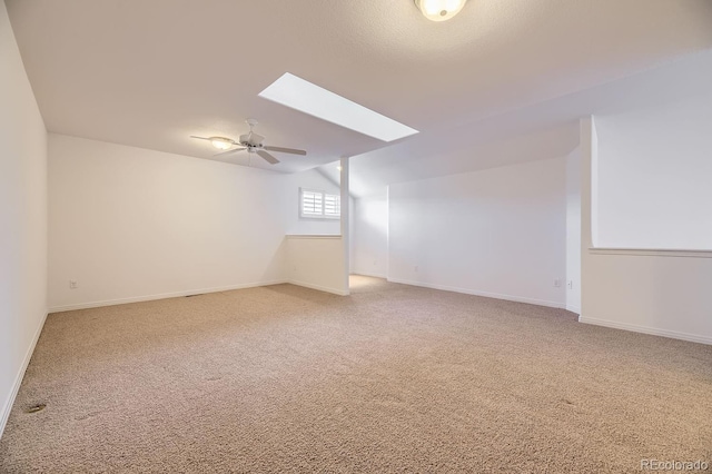 carpeted empty room featuring vaulted ceiling with skylight and ceiling fan