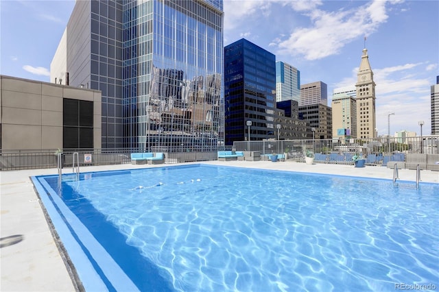 view of swimming pool featuring fence and a view of city