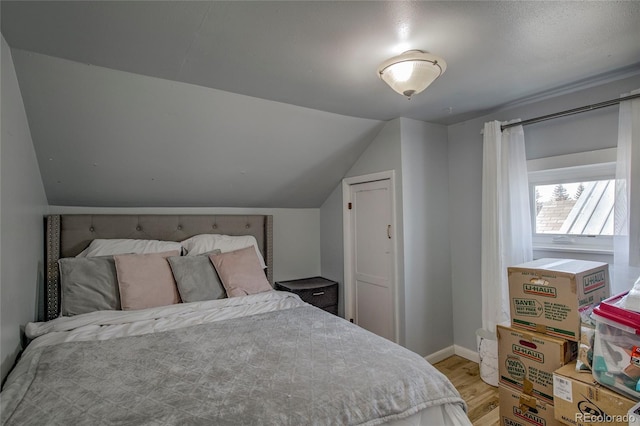 bedroom featuring light wood finished floors, baseboards, and lofted ceiling