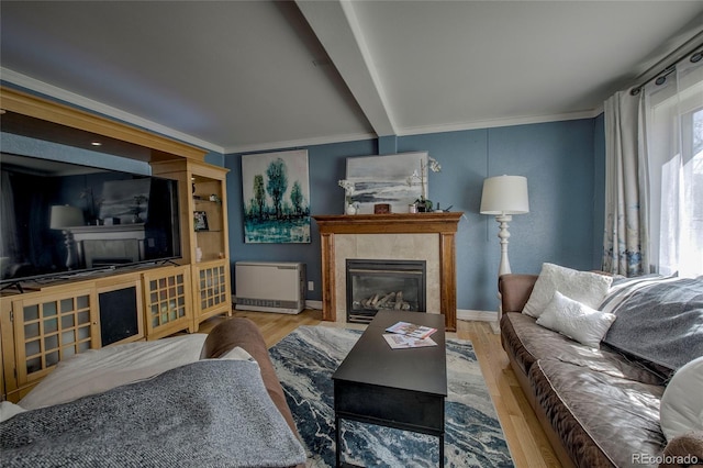 living area featuring ornamental molding, wood finished floors, a tile fireplace, baseboards, and beam ceiling