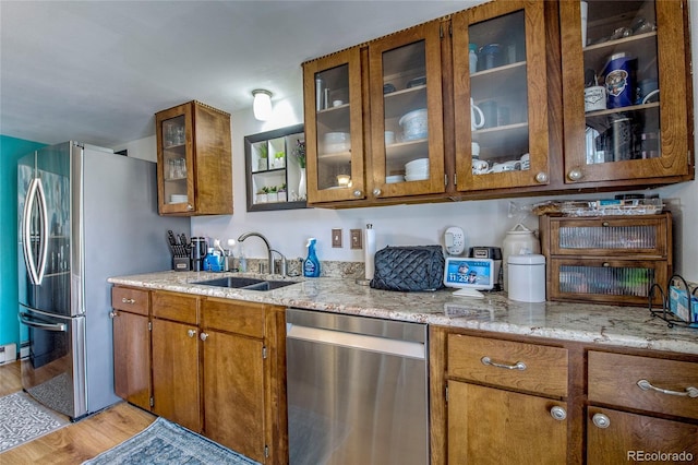 kitchen featuring brown cabinetry, light wood-style floors, appliances with stainless steel finishes, and a sink