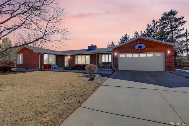 single story home with brick siding, a chimney, concrete driveway, an attached garage, and a front lawn