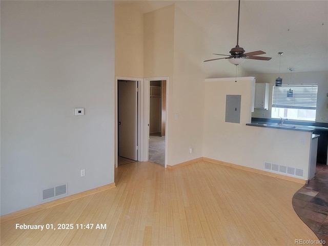 unfurnished living room with sink, electric panel, a towering ceiling, ceiling fan, and light hardwood / wood-style floors