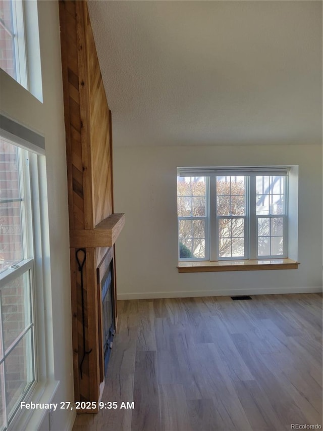 unfurnished living room featuring a glass covered fireplace, visible vents, baseboards, and wood finished floors